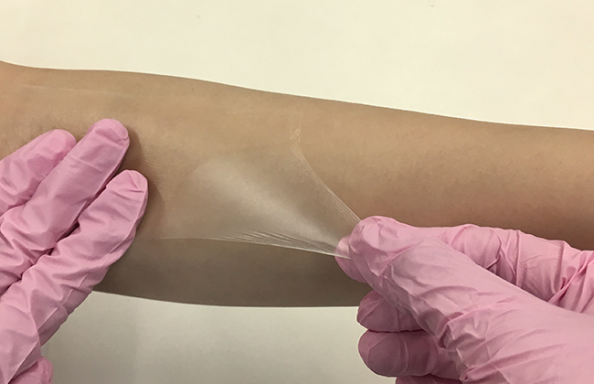 フィルムドレッシングの肌にやさしいはがし方：フィルムを肌からできるだけ浮かせず、肌と平行になるようにやさしく引っぱって伸ばしながら、ゆっくりはがします。